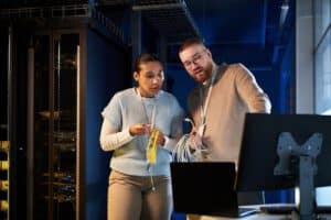 Two colleagues holding network cables, while discussing in front of a work station.
