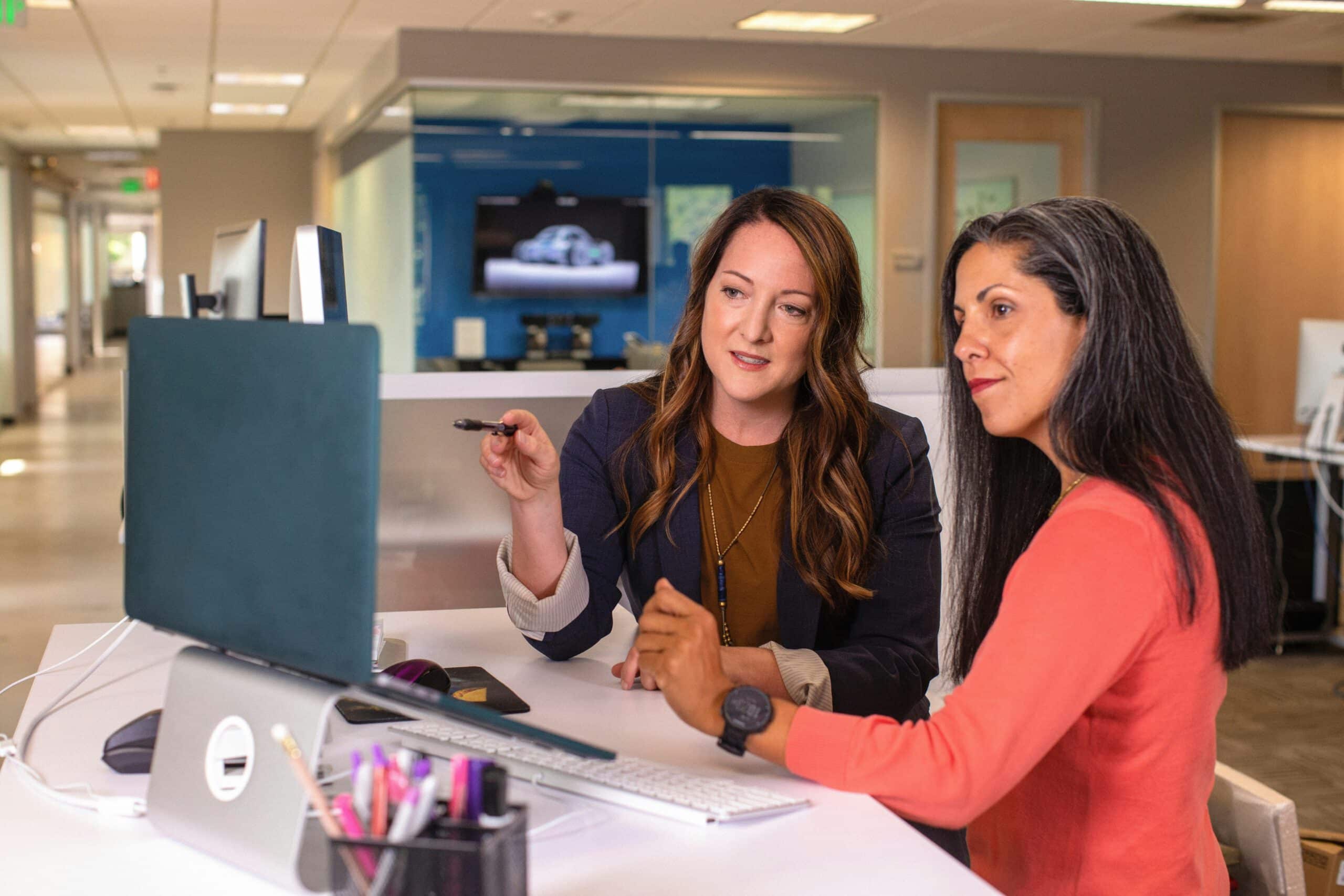 Direct shot of two people in an office discussing in front of a laptop.